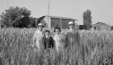 family photo taken in wheat field with farm house in background
